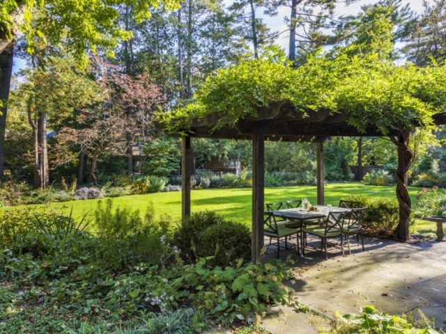 Wisteria covers a wooden pergola with a view of a lush, ellipse-shaped native perennial garden.