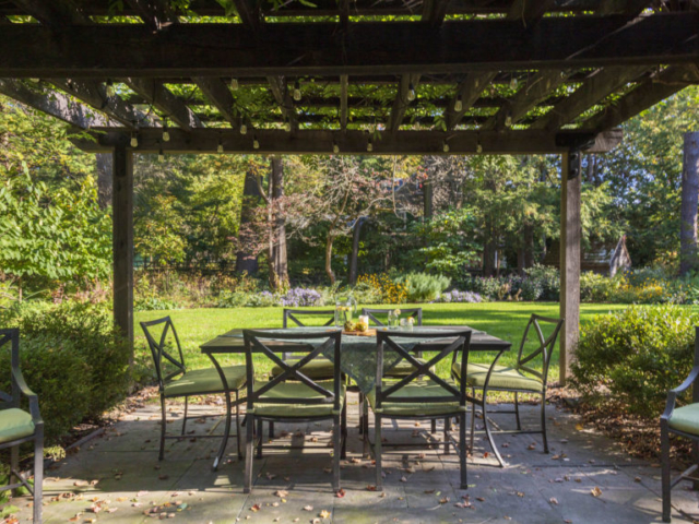 A seating area under a pergola is set for an relaxing summer afternoon.