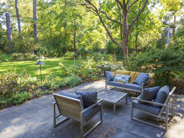 A relaxed seating area on a flagstone patio has views of a formal lawn and colorful, naturalistic garden beds.