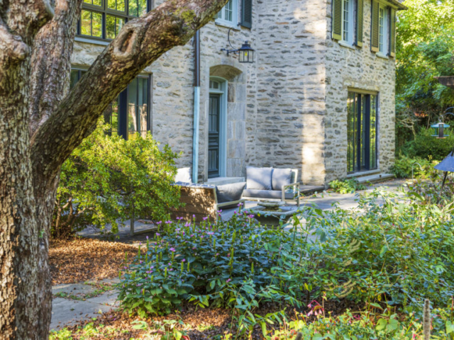 Blooming turtleheads, trees, and bird feeders surround a calm seating area on a stone patio.